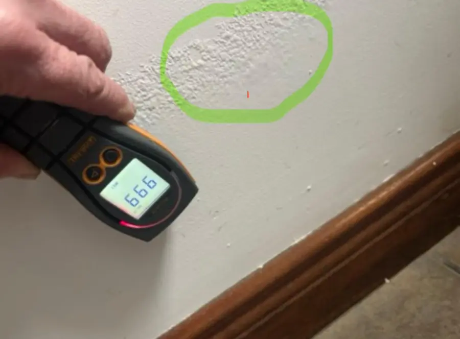 Moisture meter beside a damp patch marked with a green circle