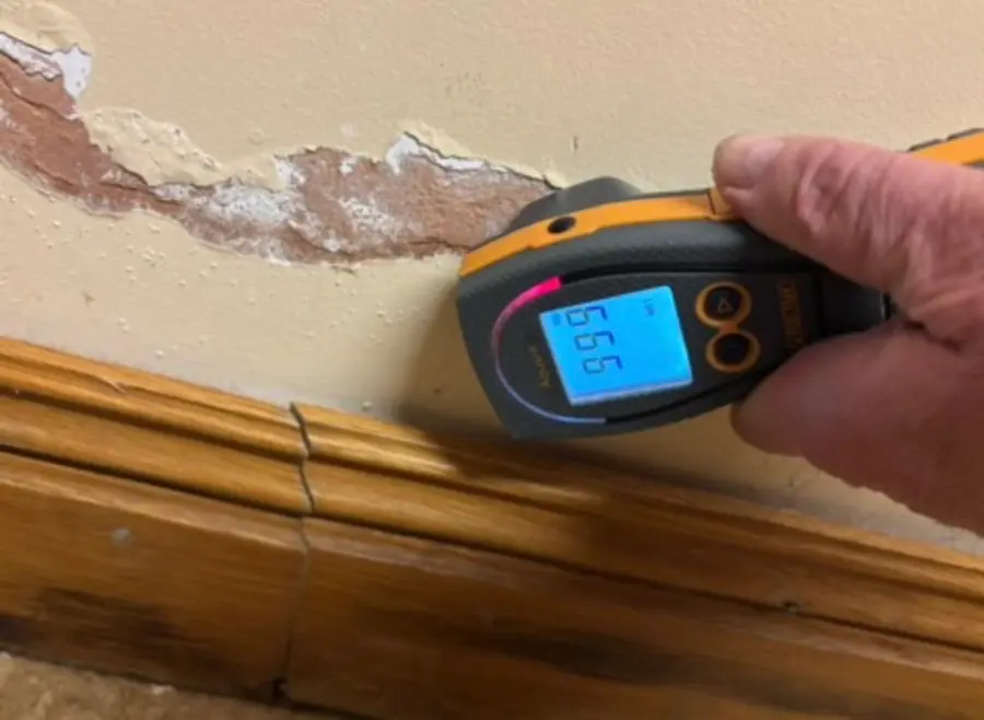 Moisture meter held against a damp wall with peeling paint