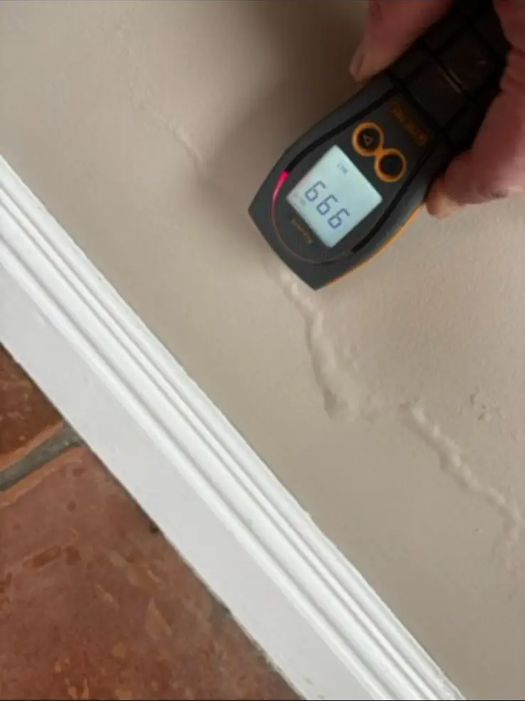 Moisture meter on a wall above a white skirting board
